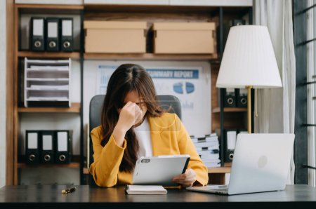 Téléchargez les photos : Frustrée jeune femme d'affaires travaillant sur une tablette et ordinateur portable assis sur le lieu de travail dans le bureau moderne - en image libre de droit