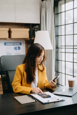 Téléchargez les photos : Confiant belle femme d'affaires asiatique dactylographier ordinateur portable et tablette numérique tout en tenant café à offic moderne - en image libre de droit