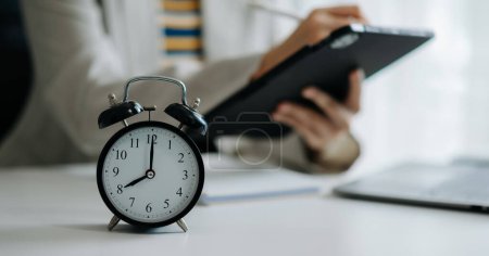 Photo for Alarm clock on the desk. Business hand using tablet  and working in modern office - Royalty Free Image
