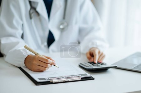 Photo for Doctor used a calculator and making notes  for medical costs at hospital - Royalty Free Image