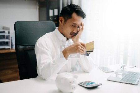 Photo for Financial owe, asian man sitting, holding credit card, stressed by calculate expense from invoice or bill - Royalty Free Image