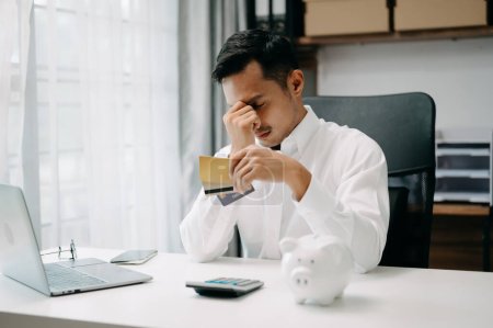Foto de Deuda financiera, hombre asiático sentado, con tarjeta de crédito, estresado por calcular el gasto de la factura o factura - Imagen libre de derechos