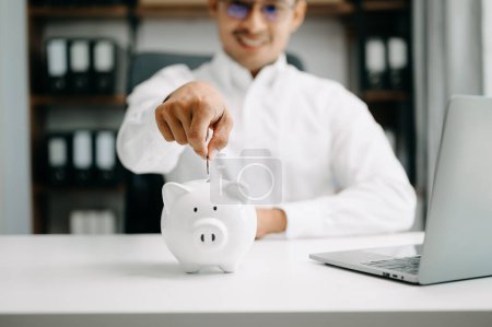 Foto de Hombre asiático están poniendo monedas en una alcancía para un negocio que crece con fines de lucro y ahorrar dinero para el futuro - Imagen libre de derechos
