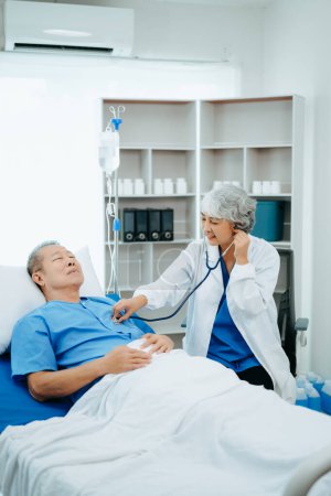 Téléchargez les photos : Asiatique médecin en costume blanc parler avec patient âgé, qui se trouve sur le lit à l'hôpital - en image libre de droit