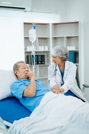 Foto de Médico asiático en traje blanco hablando con paciente anciano, que yacía en la cama en el hospital - Imagen libre de derechos
