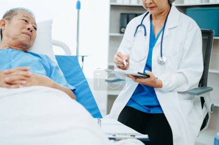 Téléchargez les photos : Médecin discutant du traitement avec un homme âgé, assis sur un lit d'examen dans une clinique ou un hôpital moderne - en image libre de droit