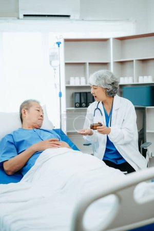 Foto de Médico asiático en traje blanco hablando con paciente anciano, que yacía en la cama en el hospital - Imagen libre de derechos