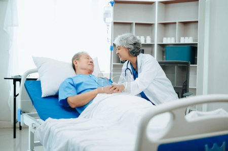 Téléchargez les photos : Asiatique médecin en costume blanc parler avec patient âgé, qui se trouve sur le lit à l'hôpital - en image libre de droit