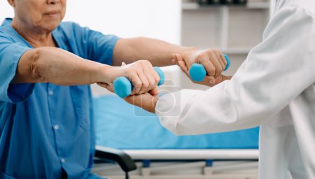 Foto de Fisioterapeuta asiática ayudar anciano paciente estiramiento brazo en hospital - Imagen libre de derechos