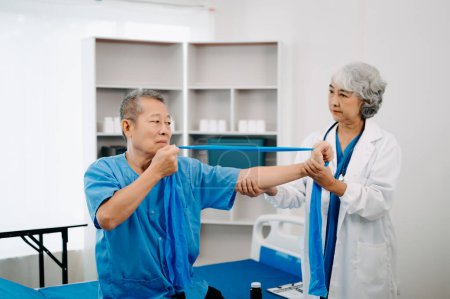 Téléchargez les photos : Asiatique physiothérapeute aider l'homme âgé patient étirement bras à l'hôpital - en image libre de droit