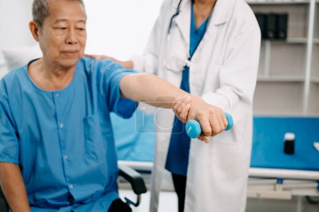 Photo for Asian physiotherapist helping elderly man patient stretching arm in hospital - Royalty Free Image