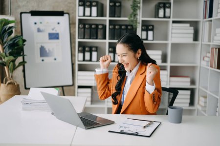 Téléchargez les photos : Heureuse femme d'affaires asiatique au travail dans le bureau avec ordinateur portable - en image libre de droit