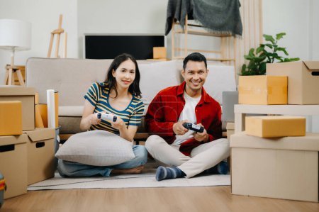 Téléchargez les photos : Asiatique jeune couple attrayant homme et femme jouer à des jeux vidéo avec des emballages en carton sur fond, déplacer dans un nouveau concept de maison - en image libre de droit