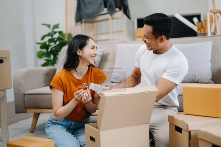 Téléchargez les photos : Jeune couple avec de grandes boîtes emménageant dans une nouvelle maison. Asiatique homme et femme aider à soulever des boîtes pour la nouvelle maison - en image libre de droit
