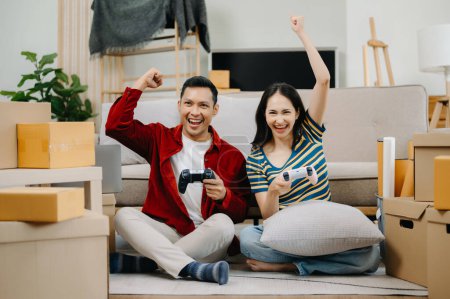 Photo for Asian young attractive couple man and woman playing video games with carton packages on background,  move in new house concept - Royalty Free Image