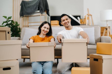 Téléchargez les photos : Heureux asiatique jeune attrayant couple homme et femme avec de grandes boîtes de déménagement dans une nouvelle maison - en image libre de droit