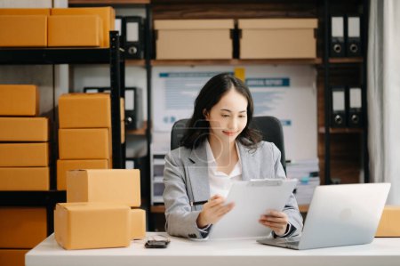 Photo for Startup small business SME,. Asian woman taking receive and checking online purchase shopping order to preparing pack product box. - Royalty Free Image