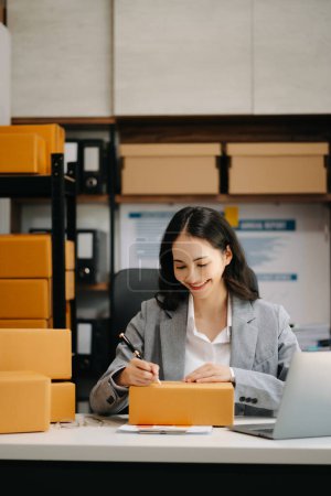 Photo for Startup small business SME,. Asian woman taking receive and checking online purchase shopping order to preparing pack product box. - Royalty Free Image