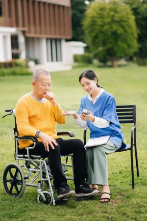 Foto de Ancianos asiático senior hombre en silla de ruedas con asiático cuidadoso cuidador y animar a paciente en jardín. - Imagen libre de derechos
