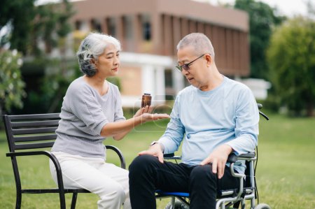 Foto de Asiático Senior hombre sentado en silla de ruedas, mujer cuidando unos de otros, momento romántico. Ellos riendo y sonriendo al aire libre en el parque - Imagen libre de derechos