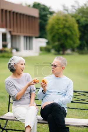 Foto de Asiática pareja de ancianos pasar un buen rato. Se ríen y sonríen mientras están sentados al aire libre en el banco del parque. Preciosa pareja de ancianos - Imagen libre de derechos
