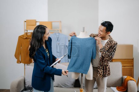 Téléchargez les photos : Couple de créateurs de mode travaillant avec des tissus et des vêtements au studio - en image libre de droit