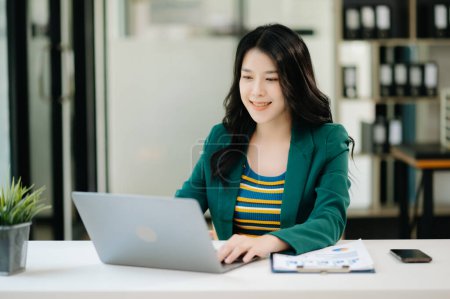 Photo for Beautiful Asian woman using laptop while sitting at her working place. Concentrated at work - Royalty Free Image