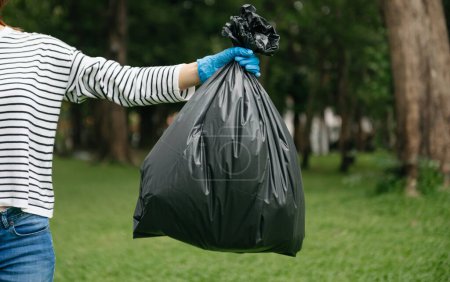 Photo for Hand holding garbage black bag putting in to trash to clean. Clearing, pollution, ecology and plastic concept - Royalty Free Image