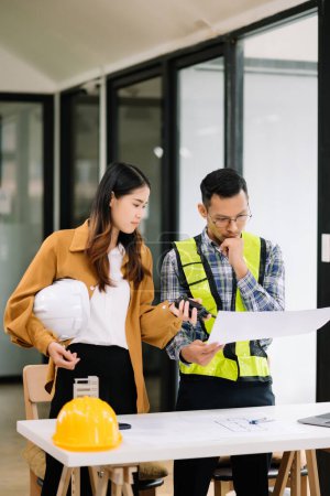 Photo for Engineer team meeting working together, wear worker vests with on architectural project site and making model house. Asian industry professional team in modern office - Royalty Free Image
