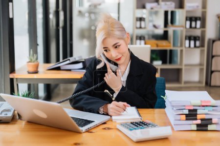 Téléchargez les photos : Heureuse femme d'affaires asiatique ont la joie de parler au téléphone et en utilisant un ordinateur portable dans le bureau - en image libre de droit