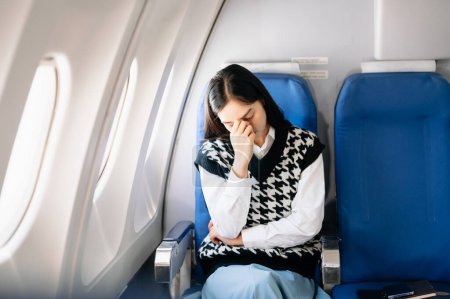 Photo for Photo of a frustrated woman sitting on an airplane with her head in her hands. Asian woman sitting in a seat in airplane - Royalty Free Image