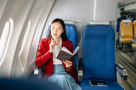 Photo for Young Asian executive excels in first class, multitasking with notebook. Travel in style, work with grace. - Royalty Free Image