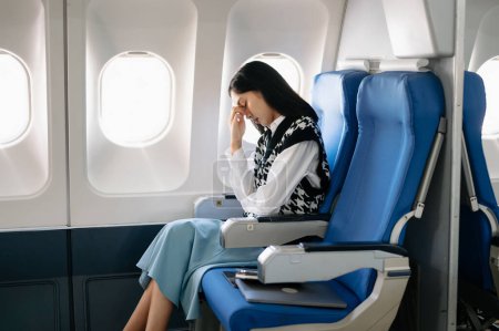 Foto de Foto de una mujer frustrada sentada en un avión con la cabeza en las manos. Mujer asiática sentada en un asiento en un avión - Imagen libre de derechos