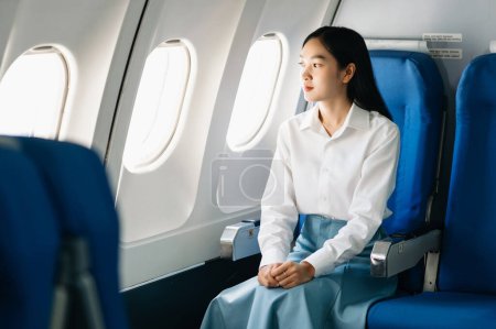 Téléchargez les photos : Femme asiatique assis dans un siège dans l'avion et regardant par la fenêtre va sur un voyage vacances concept de voyage. Capturez l'attrait de l'errance avec cette image étonnante dans le matin - en image libre de droit