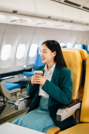Photo for Young Asian executive excels in first class with coffee. Travel in style, work with grace. - Royalty Free Image