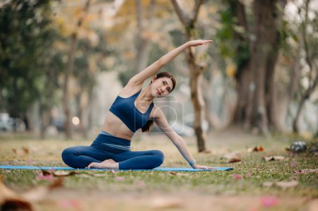 Téléchargez les photos : Portrait de jeune femme pratiquant le yoga dans un parc d'été, fond d'arbres flous. Style de vie sain et concept de relaxation - en image libre de droit