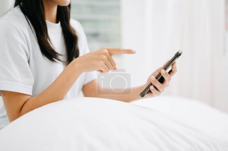 Photo for Beautiful young woman on a white bed using smartphone at home, lifestyle concept - Royalty Free Image