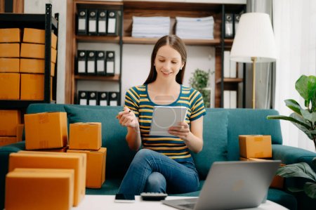 Photo for Young business owner woman prepare parcel box and check online orders for deliver to customer on laptop. Shopping Online concept. on sofa at home office - Royalty Free Image