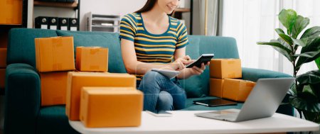 Photo for Young business owner woman prepare parcel box and check online orders for deliver to customer on laptop. Shopping Online concept. on sofa at home office - Royalty Free Image