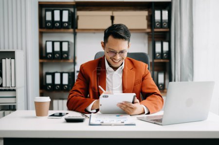 Photo for Young business man using laptop and tablet while sitting at her working place. Concentrated at work - Royalty Free Image