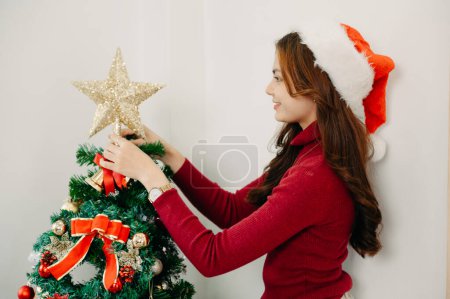 Téléchargez les photos : Femme décorant arbre de Noël avec des jouets. La lumière du soleil inonde la pièce - en image libre de droit