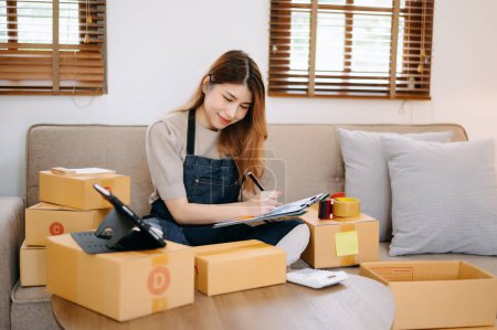 Photo for Young female business owner using laptop and preparing parcels for sending online orders to customer in home office. Shopping Online concept - Royalty Free Image