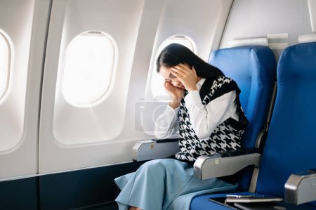 Téléchargez les photos : Photo d'une femme frustrée assise dans un avion, la tête dans les mains. Asiatique femme assis dans un siège dans l'avion - en image libre de droit