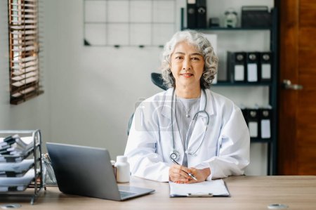 Asian smiling doctor or consultant sitting at a desk looking at the camera