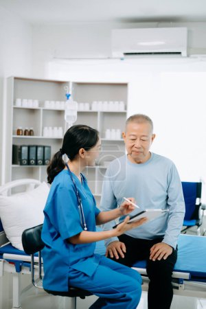 Téléchargez les photos : Médecin asiatique parlant avec un patient âgé et recevant une solution saline à l'hôpital ou à la clinique. - en image libre de droit