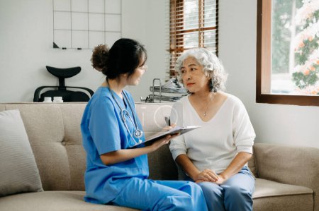 Téléchargez les photos : Asiatique soignant médecin examiner les patients âgés utilisent jauge de pression artérielle. femme thérapeute à la maison de soins infirmiers prenant soin de la femme âgée âgée assis sur le canapé.Concept de service médical le matin - en image libre de droit