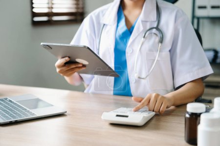 Téléchargez les photos : Médecin a utilisé une calculatrice et une tablette pour les frais médicaux à l'hôpital - en image libre de droit