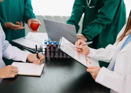 Photo for Medical team having a meeting with doctors in white lab coats and surgical scrubs seated at a table discussing a patients in the medical industry on the black desk - Royalty Free Image