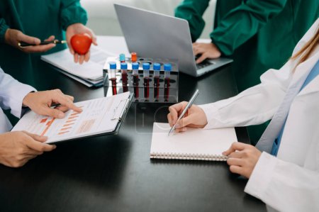 Photo for Medical team having a meeting with doctors in white lab coats and surgical scrubs seated at a table discussing a patients in the medical industry on the black desk - Royalty Free Image