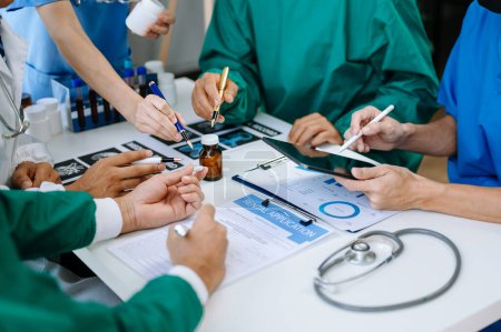 Téléchargez les photos : Équipe médicale en réunion avec des médecins en blouse blanche et en gommage chirurgical assis à une table pour discuter d'un patient travaillant en ligne à l'aide d'une tablette dans l'industrie médicale - en image libre de droit
